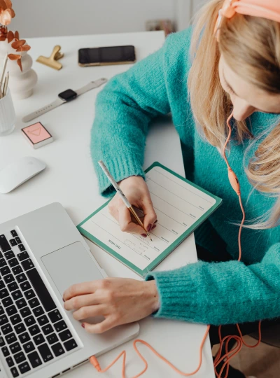 Introduction to AI portrait image Introduction to AI. female in teal coloured jumper, type with one hand and writing in a weekly planner with the other hand